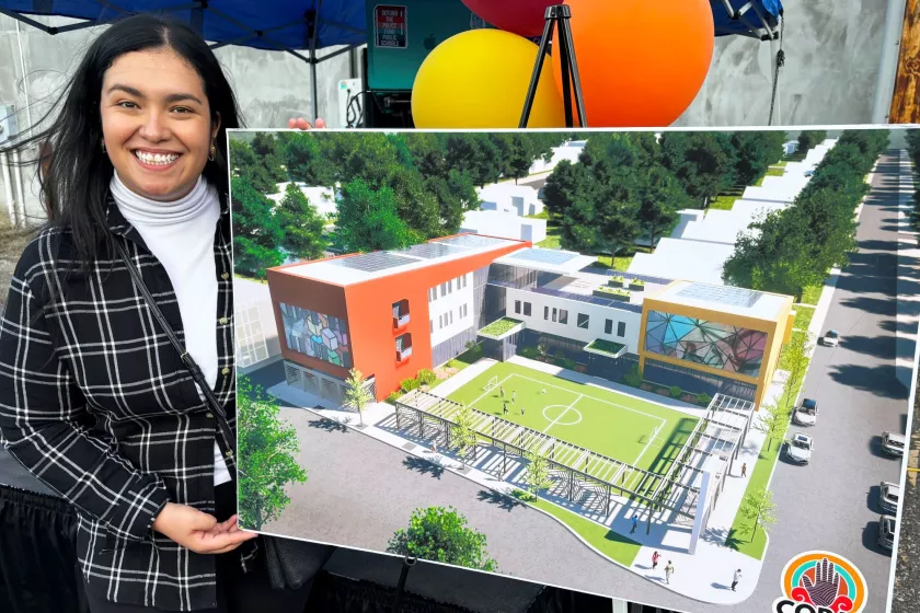 A Latina woman in her early 30's smiles at the camera. Beside her sits a large colorful poster on a stand. The image depicts a virtual rendering of a urban building, the design for the new COPAL building. 