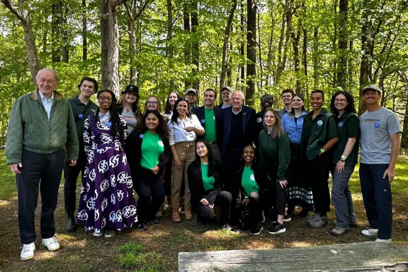 A large group of AmeriCorps stand outside alongside Alexandria Ocasio-Cortez, Bernie Sanders and Ed Markey.