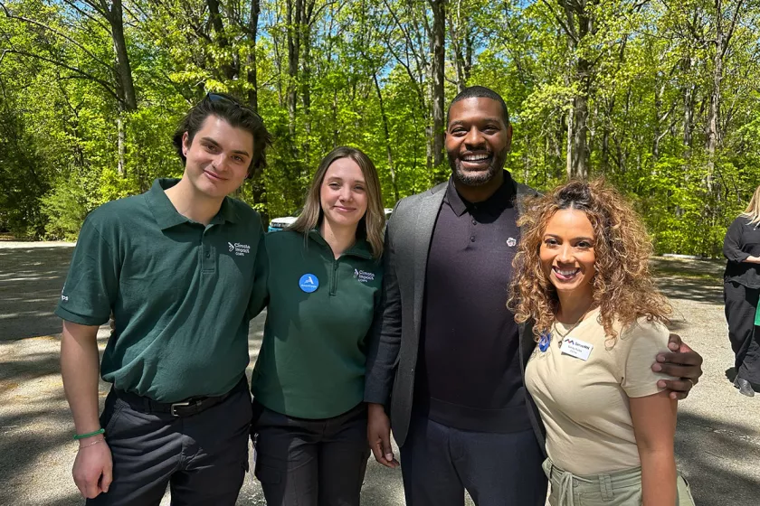 Keely Rau poses with Michael Regan and two other AmeriCorps. Green trees in background.