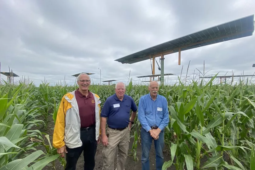  Rolly and Larry Rauenhorst and John Baumgartner stand in an open field of crops. Behind them a solar panel is propped high up.