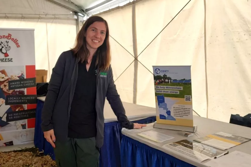 Nadya Bucklin stands leaning against a table inside a white tented area. The table displays a sign for the Clean Energy Resource Teams.