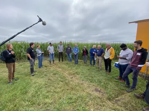 A group of people stands in a half near a field.