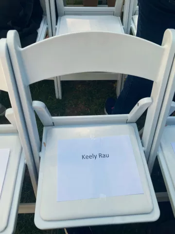 A white chair with a paper sign on the seat that says "Keely Rau."