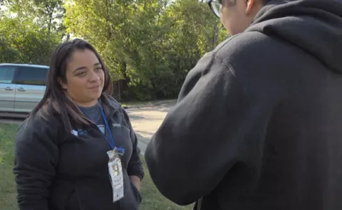 Latina woman with dark hair faces a person with their face to the camera. Trees are in background. 