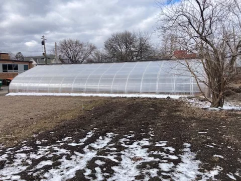 A large gray colored greenhouse surrounded by snow. 