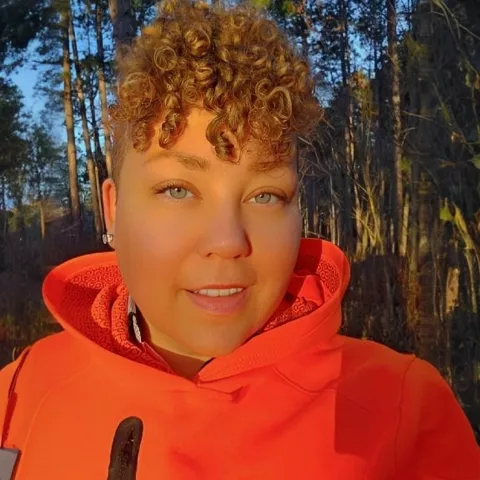 Close up shot of a woman smiling. She has golden curly hair and blue eyes.