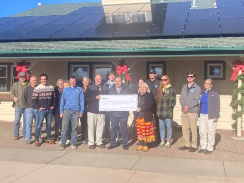 A crowd of people outdoors holding a a large check.