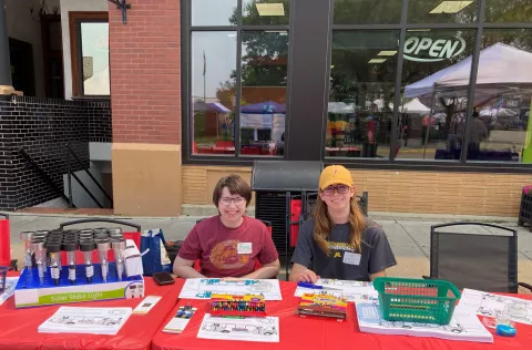 Amethyst and a fellow electrical engineering student sit outside at a table. They are working an event together. 