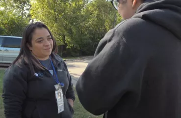 Latina woman with dark hair faces a person with their face to the camera. Trees are in background. 