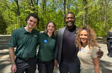 Keely Rau poses with Michael Regan and two other AmeriCorps. Green trees in background.