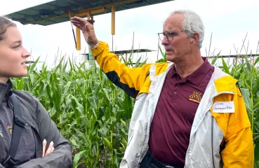 John Baumgartner stands in front of a field of crops and a large solar panel. 