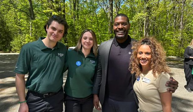 Keely Rau poses with Michael Regan and two other AmeriCorps. Green trees in background.